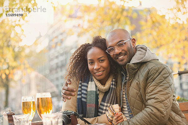 Portrait lächelndes junges Paar beim Umarmen und Biertrinken im herbstlichen Straßencafé