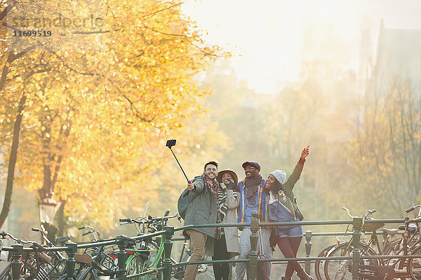 Verspielte junge Freunde nehmen Selfie mit Selfie Stick auf urbaner Herbstbrücke  Amsterdam