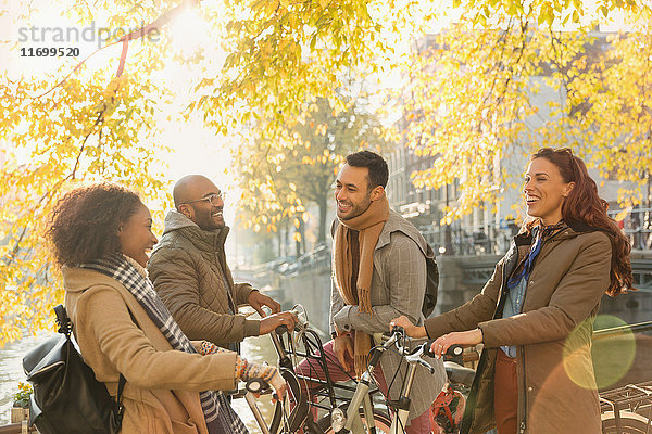 Lächelndes junges Paar Freunde mit Fahrrädern  die sich unter einem sonnigen Herbstbaum unterhalten
