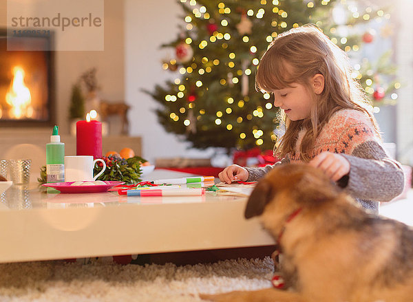 Hund beobachtet Mädchen Färbung mit Markern in Weihnachten Wohnzimmer