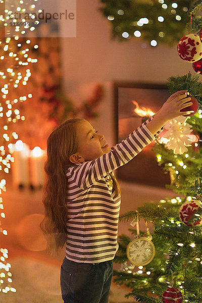 Mädchen hängt Ornament an Weihnachtsbaum