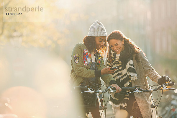 Junge Freundinnen mit Fahrrädern auf dem Handy in der sonnigen Herbststraße