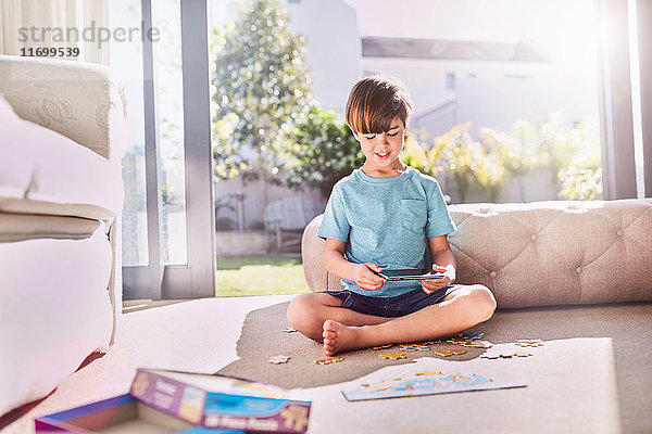 Junge mit digitalem Puzzle auf sonnigem Wohnzimmerboden