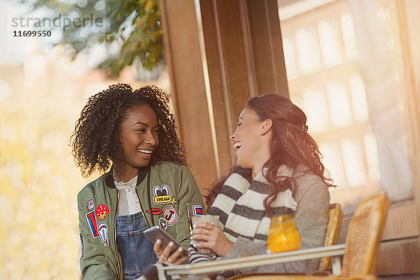 Lachende junge Frauen Freunde mit Handy im städtischen Straßencafé