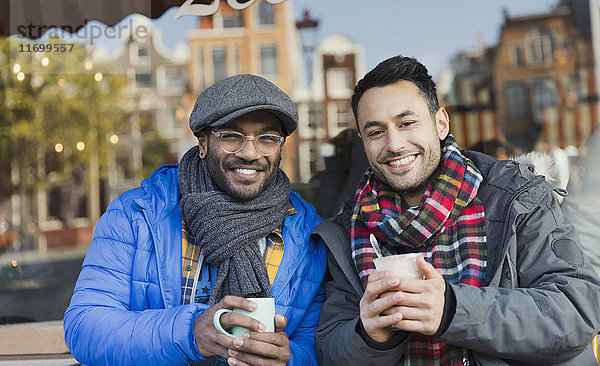 Portrait lächelnde junge Männer Freunde in warmer Kleidung trinken Kaffee in städtischen Bürgersteig Cafe