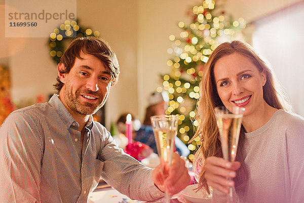 Portrait lächelndes Paar stößt mit Champagnerflöten am Weihnachtstisch an