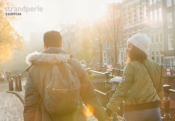 Junges Paar hält sich an den Händen und läuft auf der sonnigen Herbststraße  Amsterdam