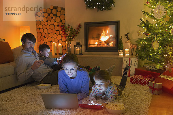 Eine Familie  die sich im weihnachtlich geschmückten Wohnzimmer mit Laptop  Tablet und Handy entspannt