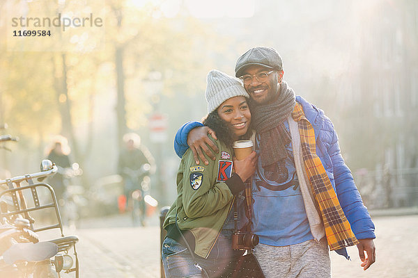 Lächelndes Paar mit Kaffeeumarmung und Spaziergang auf der urbanen Herbststraße