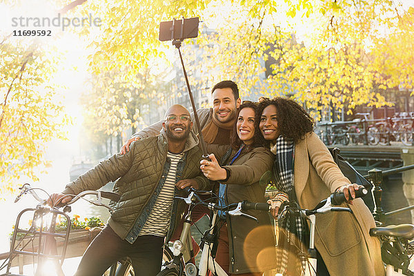 Lächelnde Freunde mit dem Fahrrad nehmen Selfie mit Selfie-Stick auf städtischer Brücke