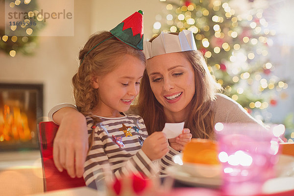 Mutter und Tochter tragen Papierkronen am Weihnachtstisch