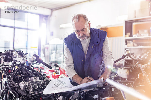 Senior Motorradmonteur bei der Überprüfung von Plänen in der Werkstatt