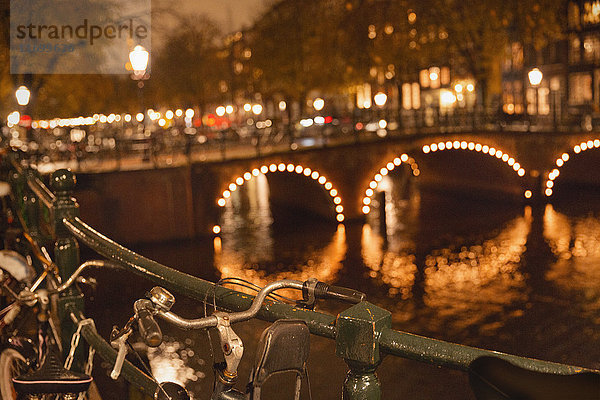 Fahrräder und Lichterketten entlang der Brücke über den Kanal bei Nacht  Amsterdam