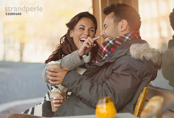 Verspieltes junges Paar mit Milchshake im Bürgersteigcafé