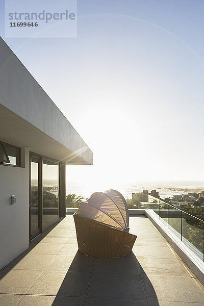 Überdachter Terrassenstuhl auf sonnigem  modernem Luxusbalkon unter blauem Himmel