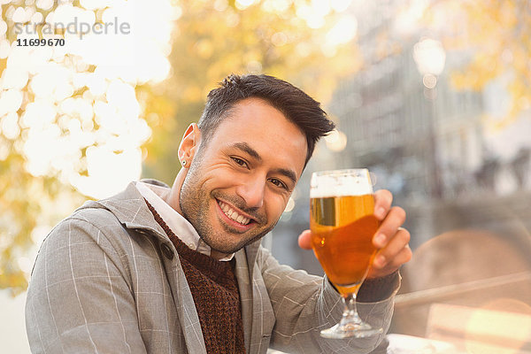 Portrait lächelnder junger Mann beim Biertrinken im herbstlichen Straßencafé
