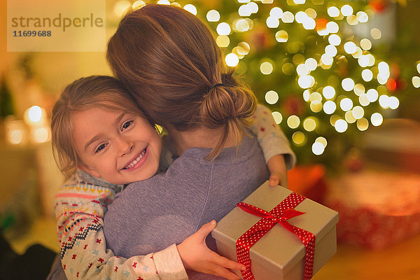 Lächelnde Tochter mit Weihnachtsgeschenk  die ihre Mutter umarmt