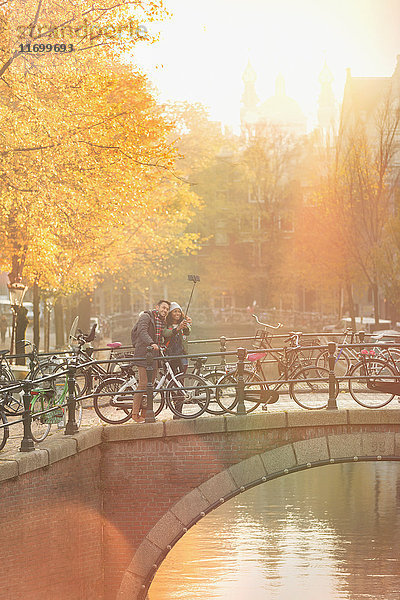 Junges Paar mit Fahrrädern nimmt Selfie mit Selfie-Stick auf Brücke über den Kanal in Amsterdam