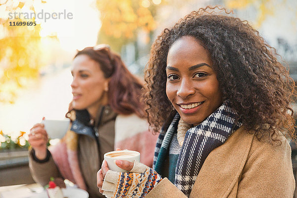Portrait lächelnde junge Frau in warmer Kleidung trinkt Espresso im Straßencafé