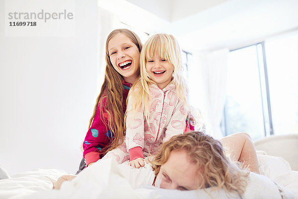 Lachende Schwestern auf Vater im Bett