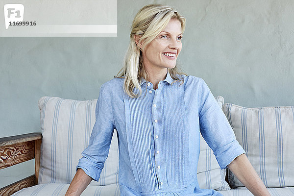 Porträt einer lächelnden  blonden Frau  die auf der Couch sitzt