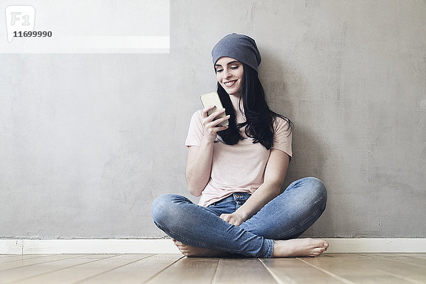 Lächelnde junge Frau auf dem Boden sitzend mit dem Handy