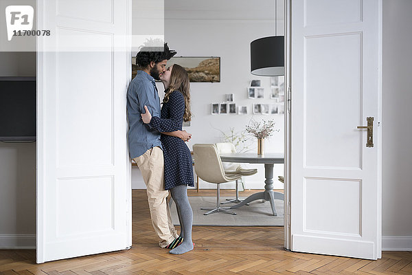 Küssendes Paar zu Hause stehend im Türrahmen im Wohnzimmer