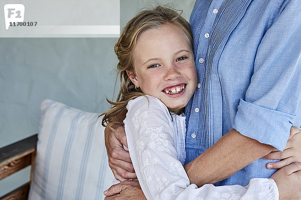 Porträt eines lächelnden kleinen Mädchens mit Zahnlücke  das seine Mutter umarmt.