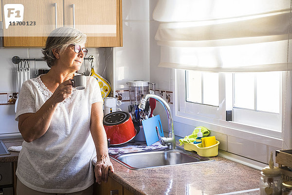 Seniorin stehend in der Küche mit einer Tasse Kaffee