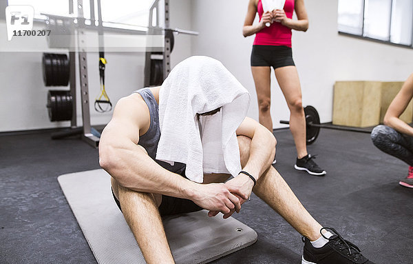 Erschöpfter Sportler mit Handtuch auf dem Kopf nach dem Training im Fitnessstudio