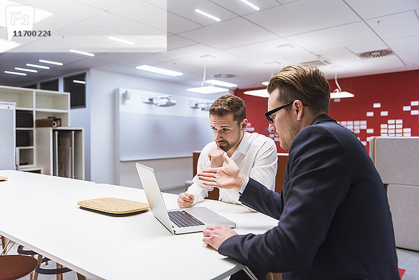 Zwei Geschäftsleute sitzen in einem modernen Büro und diskutieren vor dem Laptop.