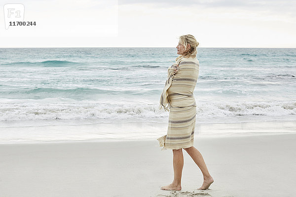 Reife Frau genießt das Meer  eingehüllt in eine Decke