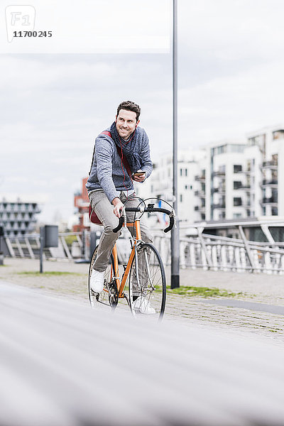 Geschäftsmann auf dem Fahrrad in der Stadt  mit Smartphone und Kopfhörer