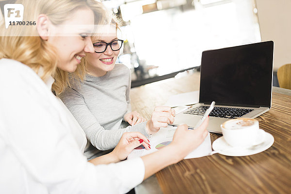 Zwei lächelnde Geschäftsfrauen arbeiten zusammen und schauen aufs Handy