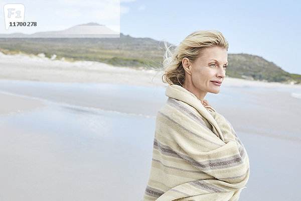 Reife Frau genießt das Meer  eingehüllt in eine Decke