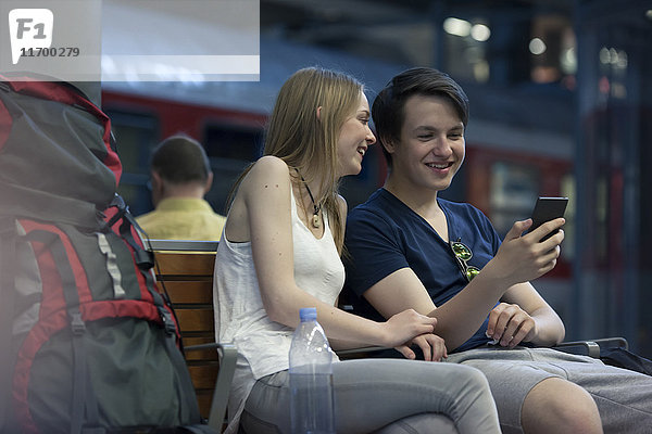 Junges Paar mit Rucksäcken am Bahnhof mit Smartphone