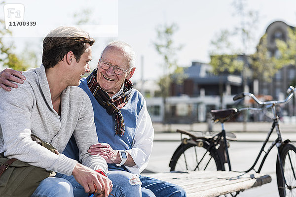 Glücklicher älterer Mann mit erwachsenem Enkel  der auf einer Bank sitzt.