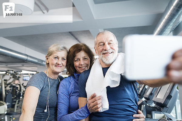 Gruppe von fit Senioren im Fitnessstudio  die nach dem Training einen Selfie mit dem Smartphone nehmen.