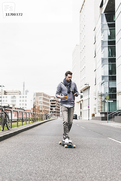 Geschäftsmann beim Skateboarden mit Smartphone und Kopfhörer