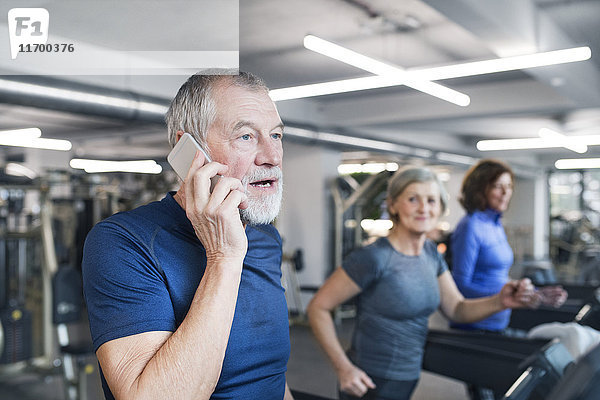 Gruppe von fit Senioren auf Laufbändern im Fitnessstudio  Mann mit Smartphone