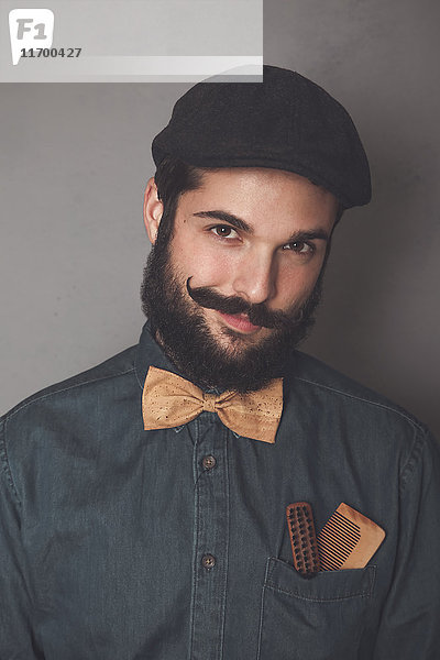 Porträt eines bärtigen Mannes mit Mütze  Jeanshemd  Kork-Fliege  Holzkamm für Bart und Schnurrbart in der Tasche.