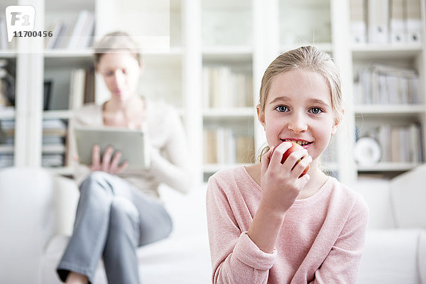 Mädchen beim Apfelessen zu Hause mit Mutter im Hintergrund