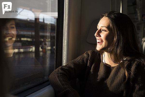 Glückliche junge Frau im Zug  die aus dem Fenster schaut.