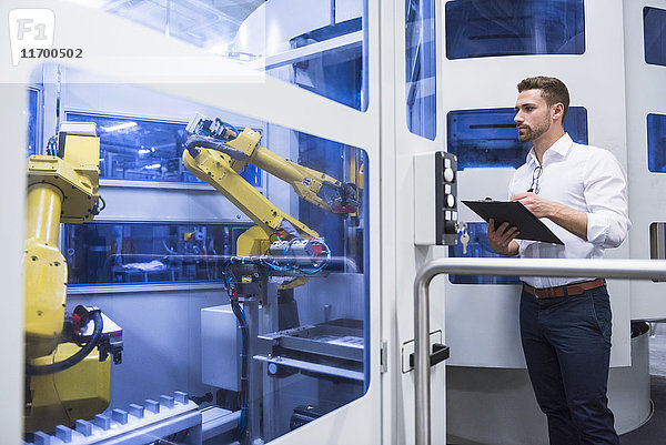 Mann macht sich Notizen an der Robotermaschine in der Fabrikhalle