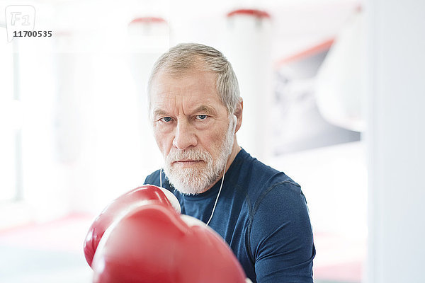 Porträt eines seriösen Senioren mit Kopfhörern und Boxhandschuhen im Fitnessstudio