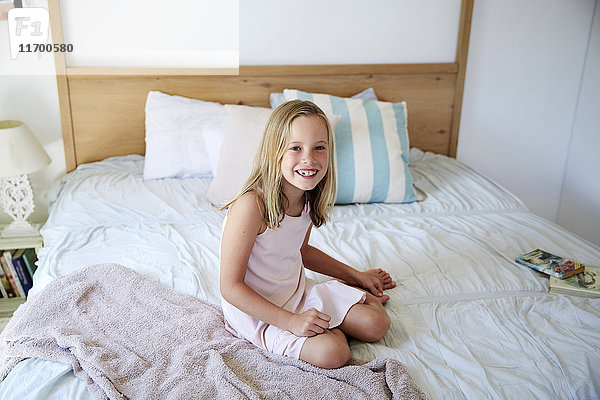 Porträt eines lächelnden kleinen Mädchens  das zu Hause auf dem Bett sitzt.