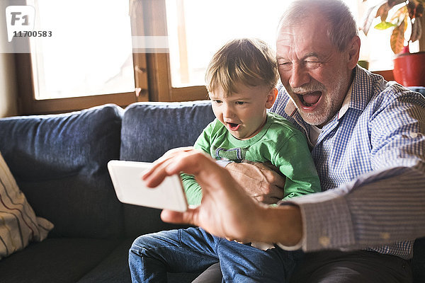 Großvater und Enkel sitzen auf der Couch und nehmen das Smartphone mit.