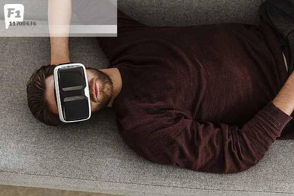 Mann auf der Couch liegend mit Virtual Reality Brille