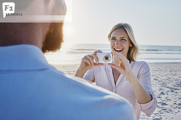 Glückliche Frau beim Fotografieren des Mannes am Strand