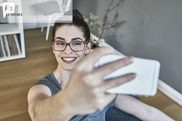 Lächelnde junge Frau nimmt einen Selfie mit nach Hause